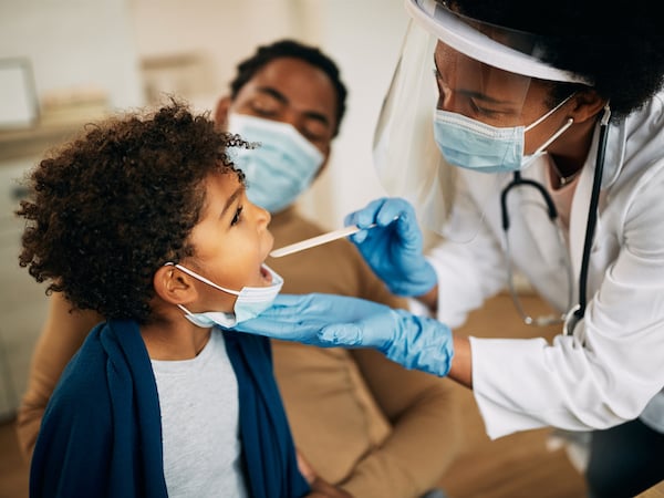 African American Doctor with a face mask examining a boys throat during a home visit