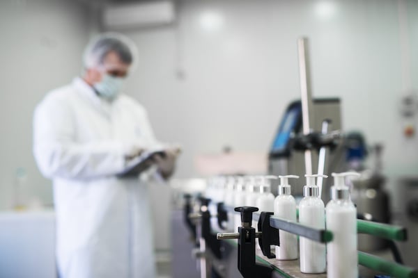 Close up of liquid soap going on a production line in front of cosmetics fabric worker typing on a tablet_Environmental Sampling