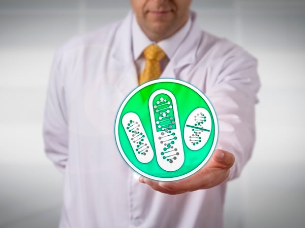 A person in a white lab coat, likely a medical professional, is holding out their hand towards the camera, presenting a large, translucent, virtual button. The button is circular with a light green background and depicts a pair of white double helix DNA strands.