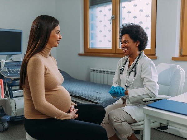 Pregnant woman sitting and talking with a smiling female doctor in a medical office.