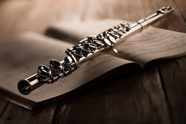  A close-up image of a silver flute resting on an open sheet of music. The focus is on the keys and body of the flute, with blurred musical notes in the background.