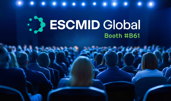 A large audience is seated in a dimly lit conference hall, facing a stage illuminated by bright blue lights. The text 'ESCMID Global' appears prominently in white and teal, accompanied by 'Booth #B61' in green.