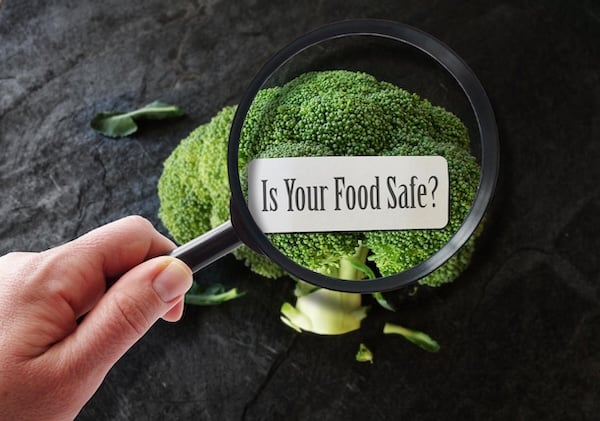 Close-up image of broccoli under a magnifying glass revealing the text, 'Is Your Food Safe?' – an exploration into food safety.