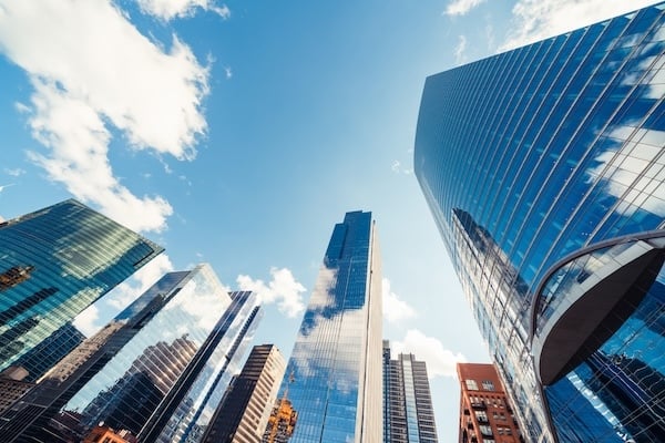 Wide-angle view of modern skyscrapers in downtown Chicago on a clear day. The buildings reflect the blue sky and white clouds, creating a bright, futuristic cityscape.
